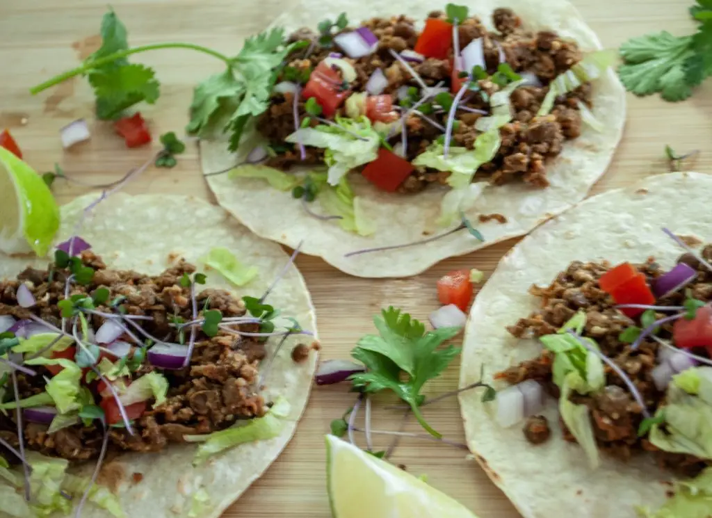 3 tacos on a platter with Easy Vegan Taco Meat, lettuce, tomato and microgreens